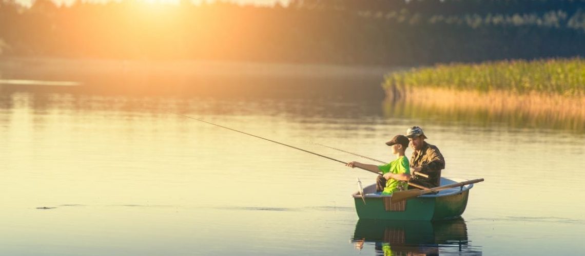 father and son catch fish from a boat at sunset