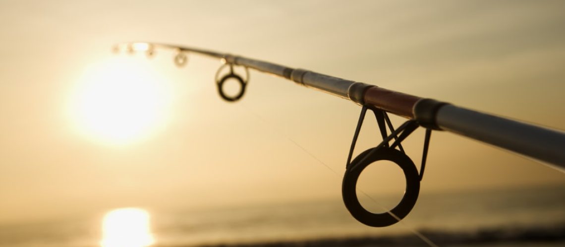 Fishing pole against ocean at sunset.